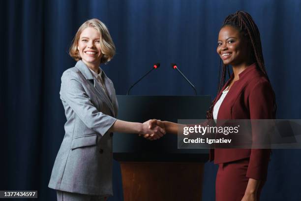 young beautiful female politicians shaking hands on camera with smiles - foreign affairs stock pictures, royalty-free photos & images