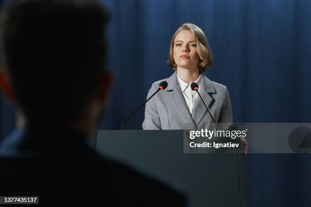 a young american female politician during the speech at the debates standing on a stage behind a pedestal on a blue background - microphone debate stock pictures, royalty-free photos & images