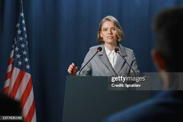a young pleasant female politician during the speech at the debates standing on a blue background - foreign affairs ministers meeting stock pictures, royalty-free photos & images