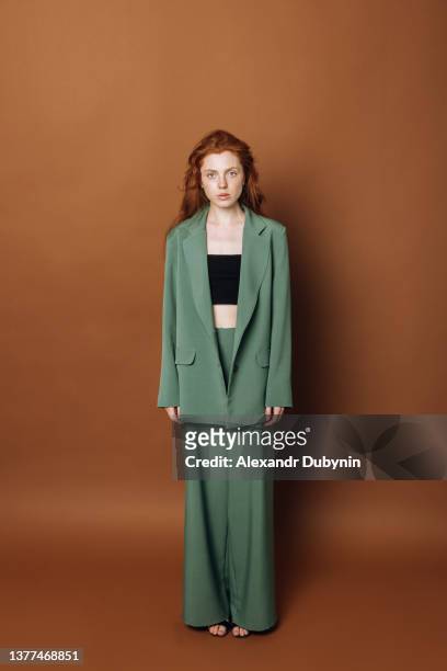 beautiful caucasian woman fashion model poses in the studio looking at the camera in a new collection of clothes. girl posing on a colored brown background in a green suit. clothing sale concept - brown suit 個照片及圖片檔