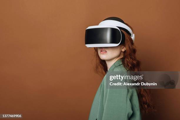 horizontal portrait of a young woman in a virtual reality helmet on a colored brown background in the studio. lady in 3d vr glasses with copy space. - virtual stock-fotos und bilder