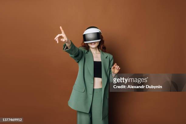 beautiful young happy caucasian woman in a virtual reality helmet on a colored brown background in the studio. smile lady with glasses vr. concept of technology and development. - casques réalité virtuelle photos et images de collection
