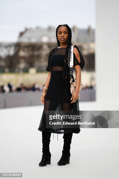 Guest wears silver earrings, a black shoulder-off cropped top, high waist black cyclist shorts, a black cut-out transparent puffy sleeves midi dress,...