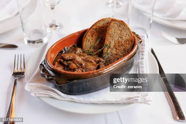 meat stew in traditional oval pottery with toasted bread slices on restaurant table - stoofvlees stockfoto's en -beelden