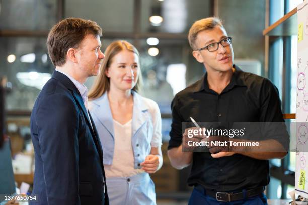 time, budget, and quality in a business project management. shot of a male business project leader in a project meeting while discussion of a budget and time frame on whiteboard to his team member in a business office. - presentation to customers stockfoto's en -beelden