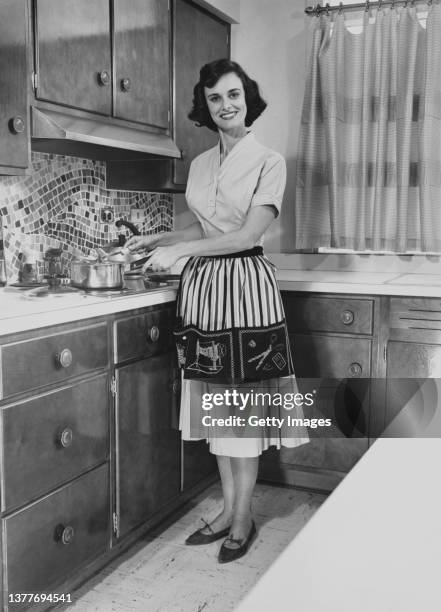 woman wearing apron cooking on hobs - fünfziger jahre stock-fotos und bilder