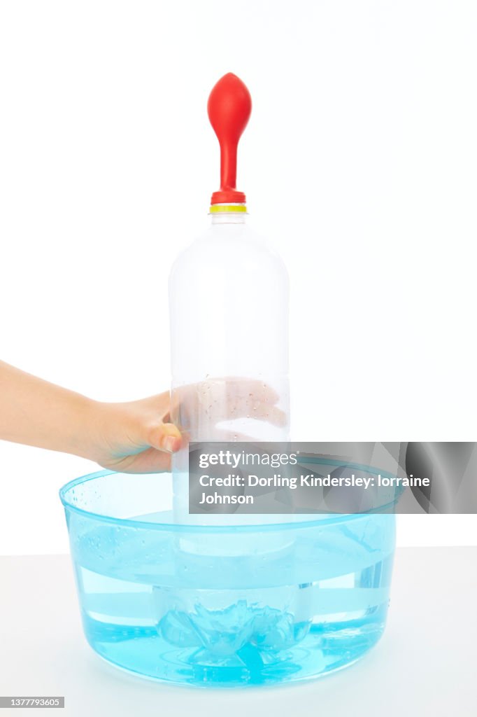 Plastic botte with red balloon over the top, sitting inside a container of water