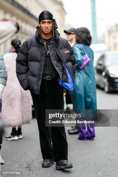 Guest wears black scarf, a black t-shirt, a black oversized puffer jacket from Calvin Klein, a black embossed print pattern shirt, black large velvet...