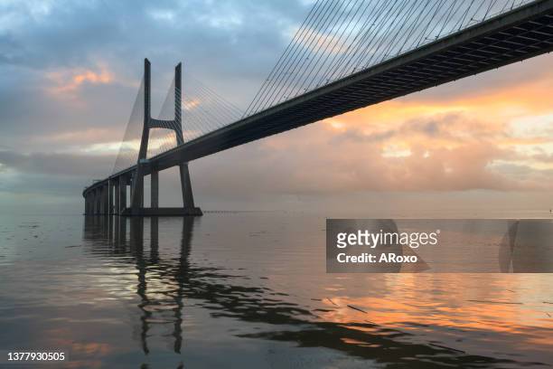 the vasco da gama bridge crosses the tagus river, and is one of the longest bridges in the world. lisbon is an amazing tourist destination because their urban landscapes, by its light, its monuments. - ponte vasco da gama stock-fotos und bilder