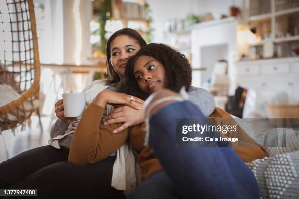 affectionate mother and daughter cuddling on sofa - family on couch with mugs stock-fotos und bilder