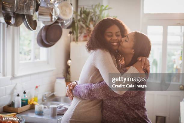 mother and daughter hugging and kissing in kitchen - mother and daughter hugging stock pictures, royalty-free photos & images