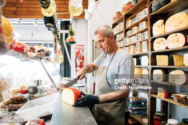 quesero que atiende los pedidos de los clientes - hombre cortando queso fotografías e imágenes de stock