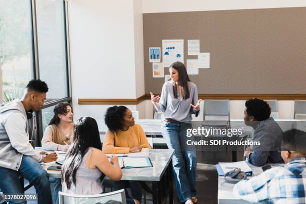 female teacher leans against table and leads group discussion - high school stockfoto's en -beelden