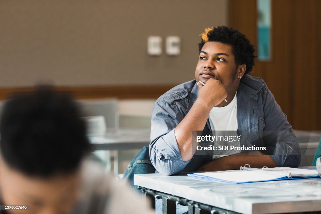 Teen boy rests chin on hand and daydreams in class