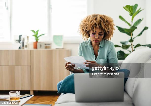 portrait of a beautiful woman looking at a document while working on her laptop - pay day stock pictures, royalty-free photos & images