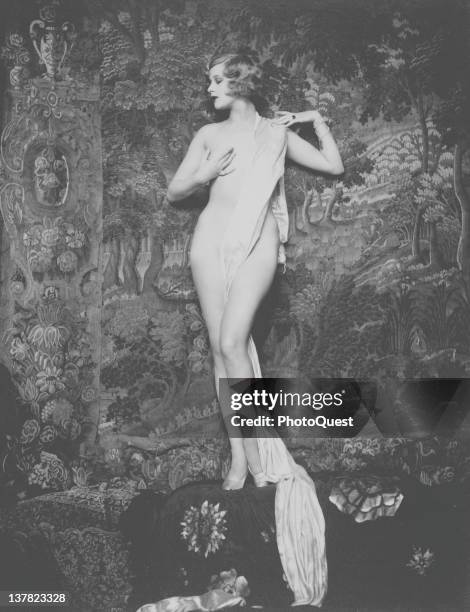 Portrait of American actress and entertainer Hazel Forbes as she poses naked except for jewelry, heels, and a strategically placed sash, late 1920s.