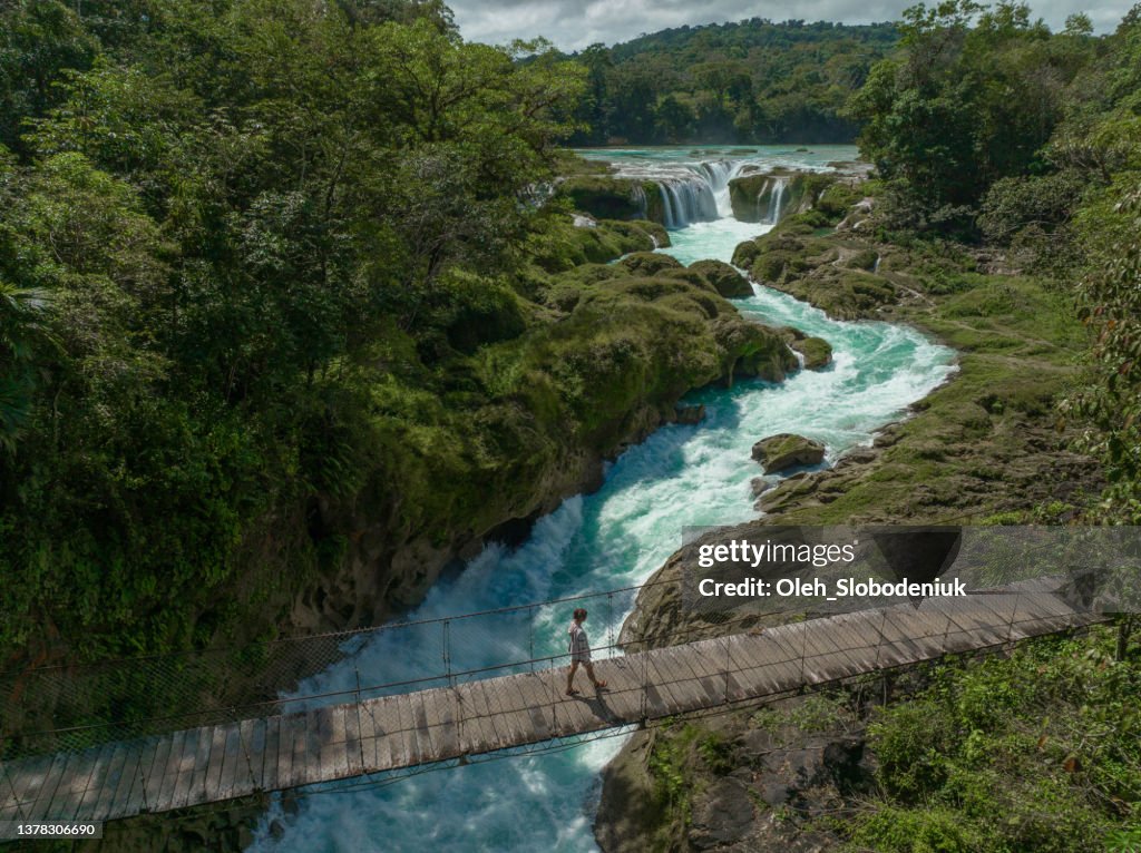 Aerial view of woman walking on suspension bridge over Las Nubes waterfall in Chiapas