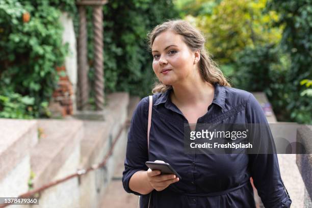 beautiful plus size woman standing in the park and using her smartphone while waiting for a friend - morbidly obese woman 個照片及圖片檔