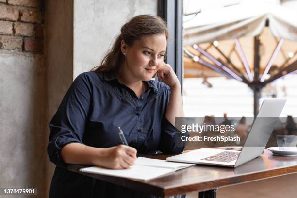 donna d'affari caucasica in sovrappeso felice seduta in un bar© e che lavora sul suo laptop - corporatura larga foto e immagini stock