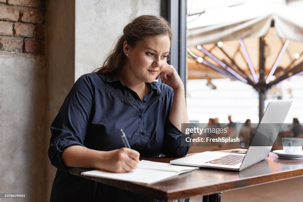 Happy Caucasian Overweight Businesswoman Sitting at a Café and Working on her Laptop