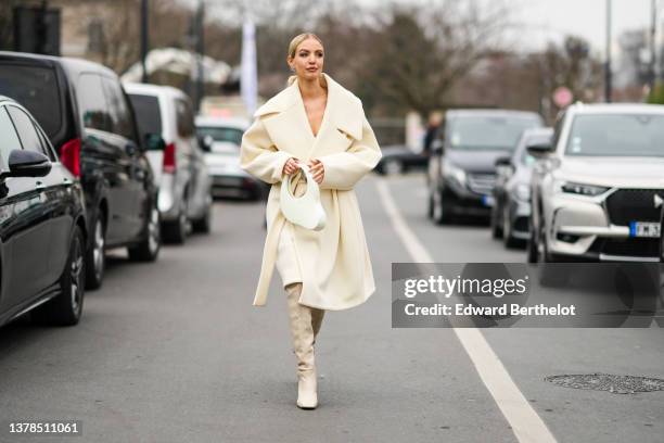 Leonie Hanne wears silver and rhinestones earrings from Balenciaga, a white latte oversized long belted coat, a white Melted Swipe handbag from...
