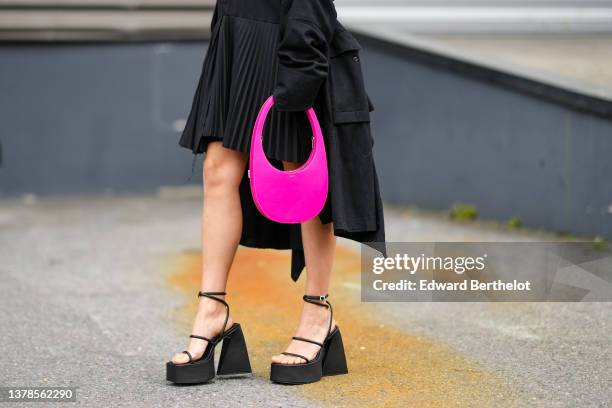 Regina Anikiy wears a black blazer shirt / pleated skirt dress from Coperni, a black long coat, a neon pink shiny leather handbag from Coperni, black...