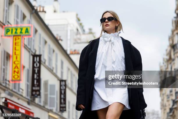 Influencer Alessa Winter wearing a white mini dress by Patou, a white bluse with bow and ruffles by Patou, a long black coat by The Frankie Shop and...