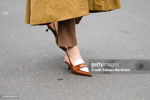 Caroline Issa wears a brown yellow mustard high neck / belted / long coat, brown suit pants, white leather and camel varnished leather pointed heels...