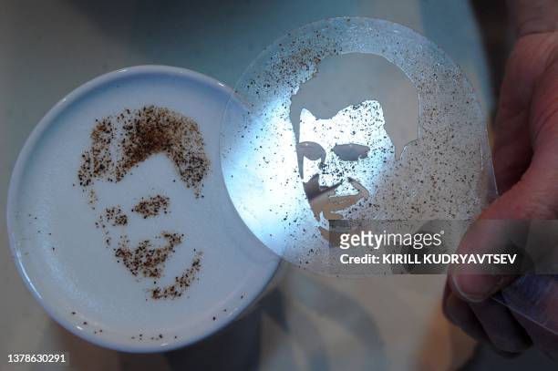 Barista uses a stencil to create a portrait of presidential candidate Mikhail Prokhorov with cinnamon and cocoa powder sprinkled on the foam of a...