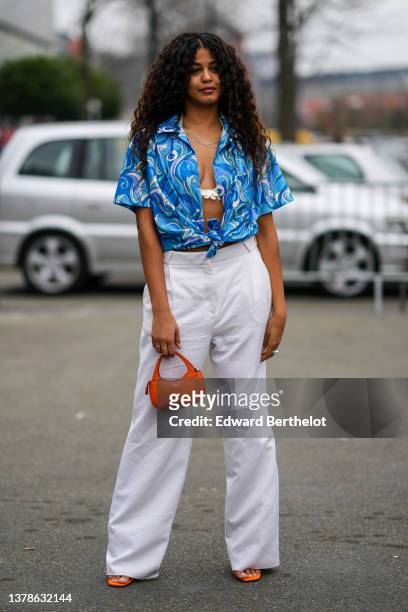 Guest wears gold and silver chain necklaces, a blue / purple / green / white print pattern short sleeves / knot / open shirt from Coperni, a white...