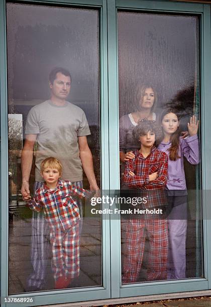 family in pyjamas' looking out rainy window - standing in the rain girl stockfoto's en -beelden