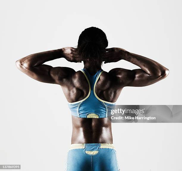 athletic black female tensing back muscles - sportlerin stock-fotos und bilder