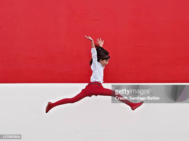 girl jumping in air at red wall - children jumping stock-fotos und bilder