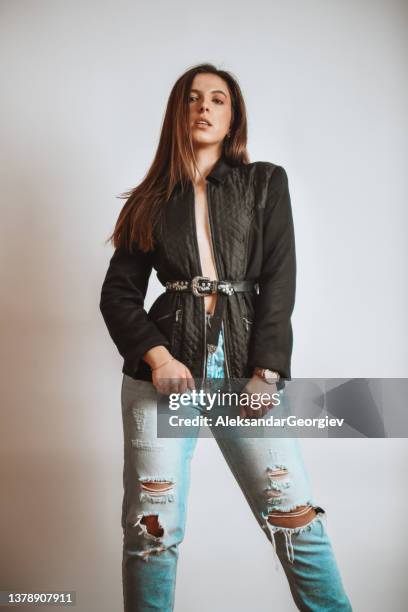 beautiful female showcasing new jacket with ripped jeans on studio background - ripped jeans stock pictures, royalty-free photos & images