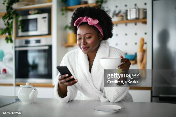 hermosa joven, bebiendo té y usando su teléfono. - bathrobe fotografías e imágenes de stock