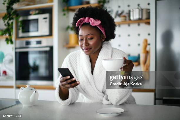 beautiful young woman, drinking tea and using her phone. - indulgence stock pictures, royalty-free photos & images