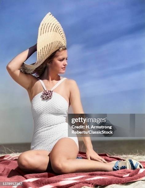 1930s 1940s Woman In White Bathing Suit Sitting On Beach Wearing Big Straw Hat.