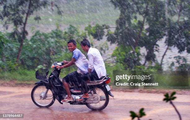 Two young men ride on a motorcycle passing the Khmer Monastic Temple Complex of Banteay Chhmar,Banteay Meanchey, Cambodia on May 25, 2012.. The rainy...