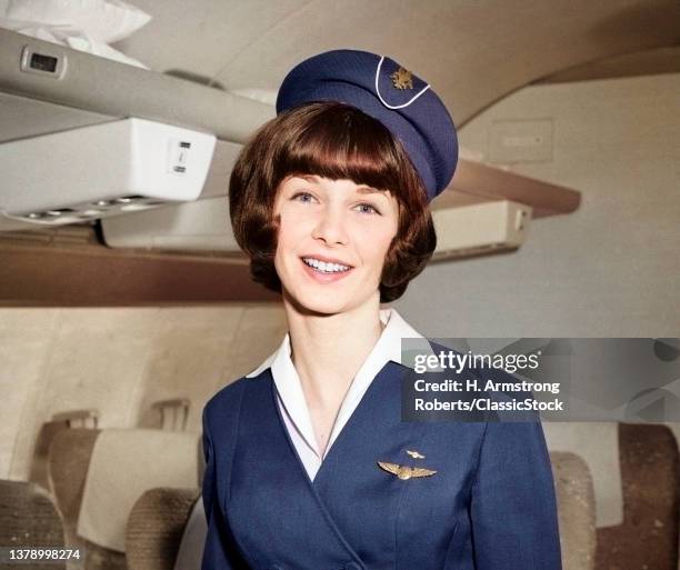 1960s Smiling Portrait Of Airline Stewardess In Airplane Aisle Looking at Camera.