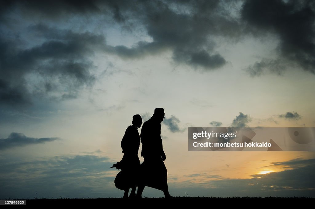 Two men walking on beach at sunset