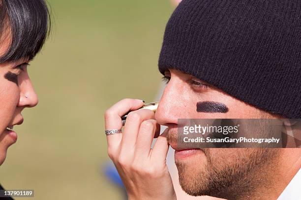 woman applies eye black grease under man eyes - eye black fotografías e imágenes de stock
