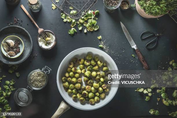 roasted green brussels sprouts in white cooking pan with ingredients on black kitchen table. - brussels sprout stock-fotos und bilder