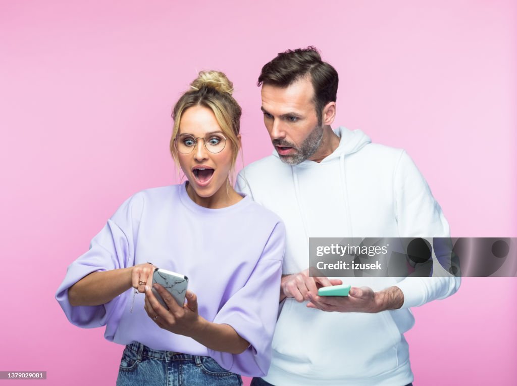 Surprised mid adult couple sharing smart phone
