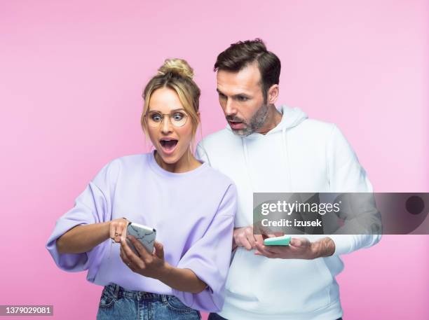 surprised mid adult couple sharing smart phone - couple studio shot stock pictures, royalty-free photos & images