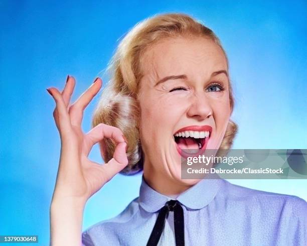 1950s Enthusiastic Blond Woman Mouth Open Winking Eye Looking At Camera And Making Ok Sign With Thumb And Finger.