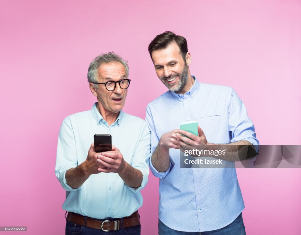 Happy man sharing smart phone with senior father