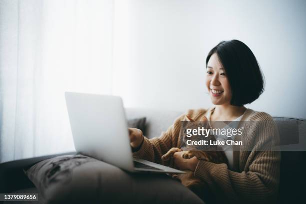 cheerful young asian woman browsing the internet with her cat at home during the pandemic time - cat laptop stockfoto's en -beelden