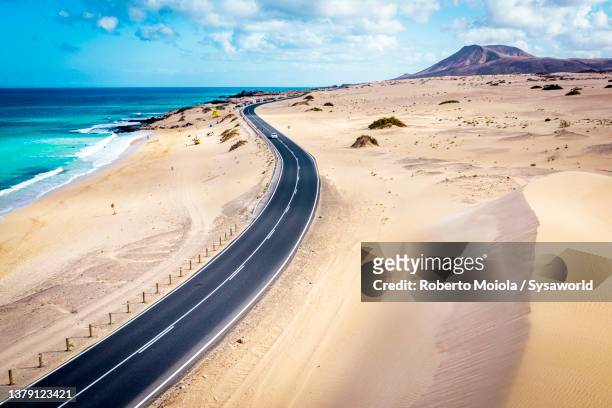 empty desert road beside sand dunes and ocean - corralejo stock-fotos und bilder