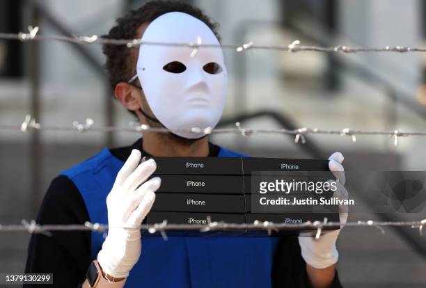 An activist with the group SumOfUs holds a stack of iPhone boxes as he wears a costume depicting Uyghurs in a mock forced labor camp as he stages a...