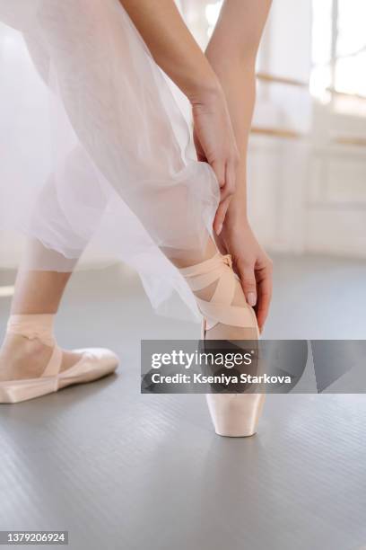 young european woman practices ballet touches pointe shoes with her hands in a tutu skirt in the studio - ballet dancers russia stock pictures, royalty-free photos & images